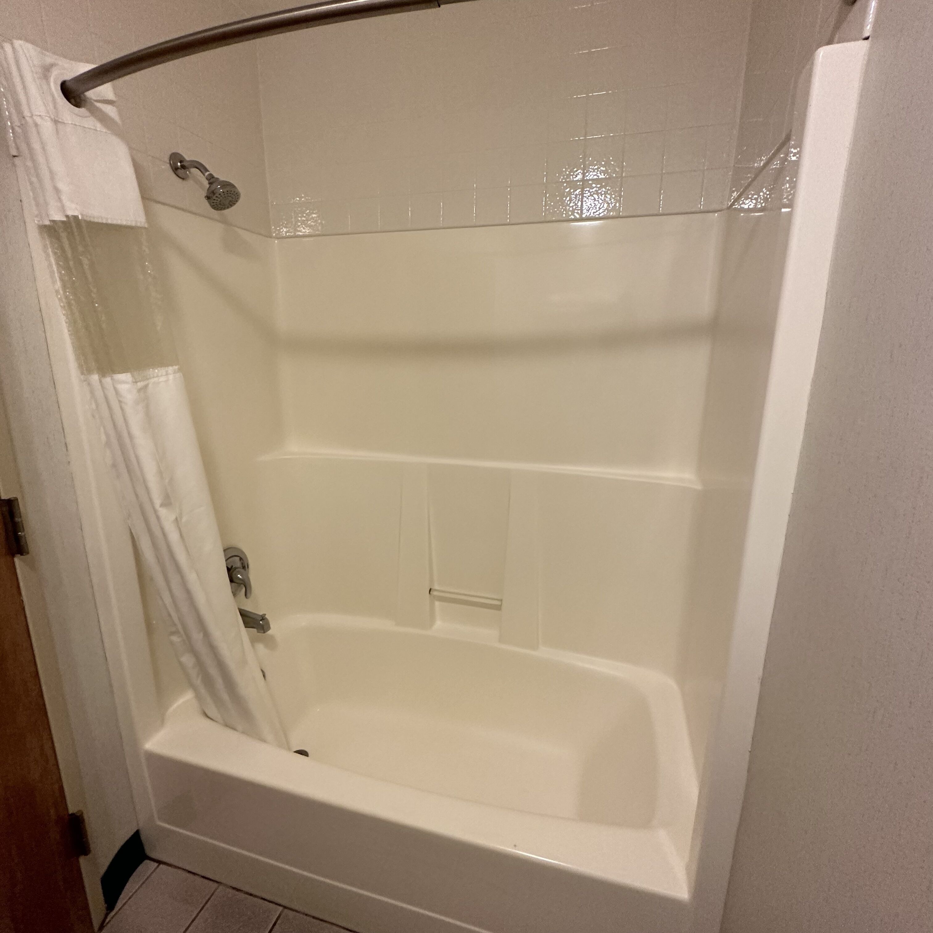 Une baignoire blanche avec un pommeau de douche, un rideau et un mur carrelé.