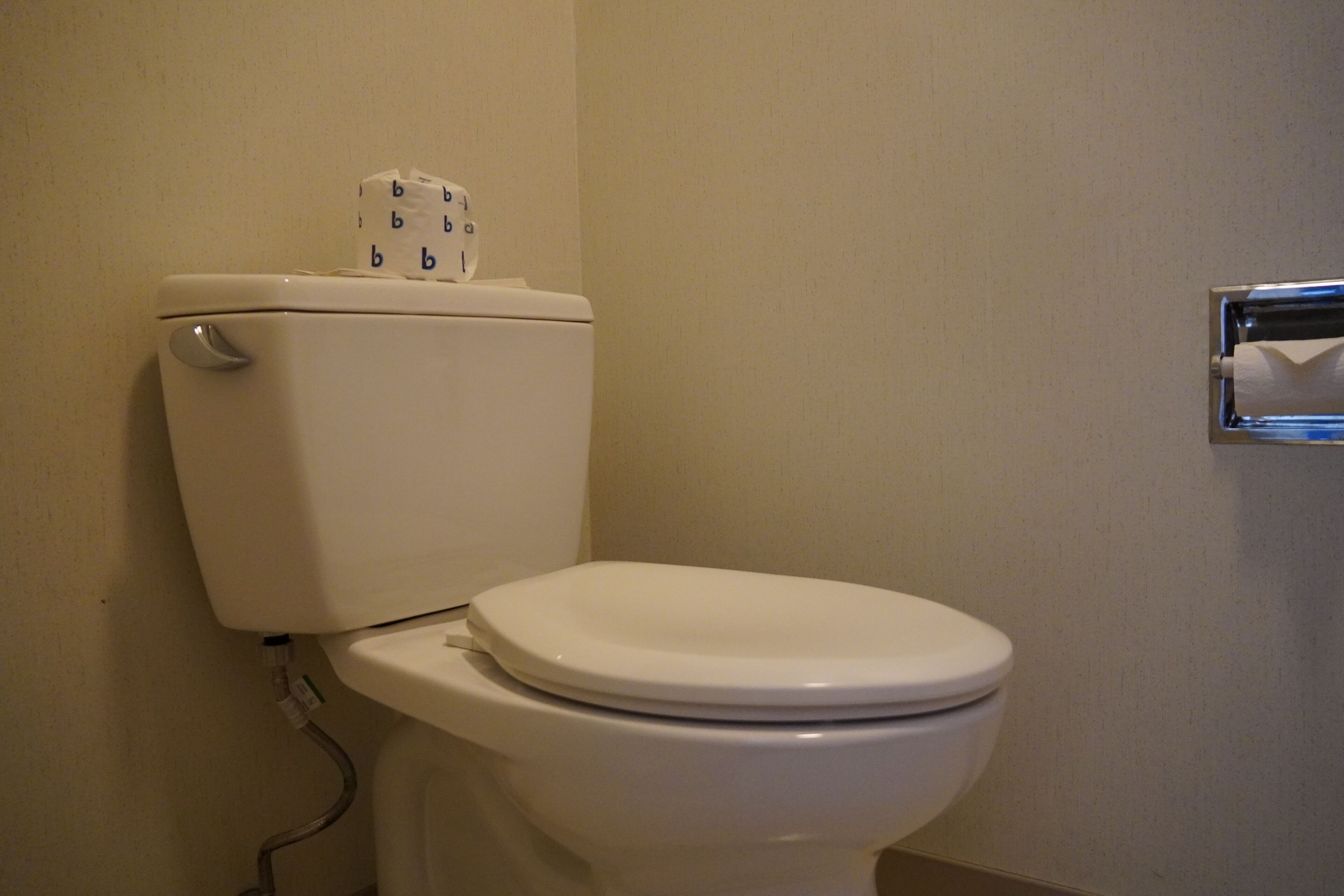 A white toilet with a paper towel holder on top and a visible pipe.
