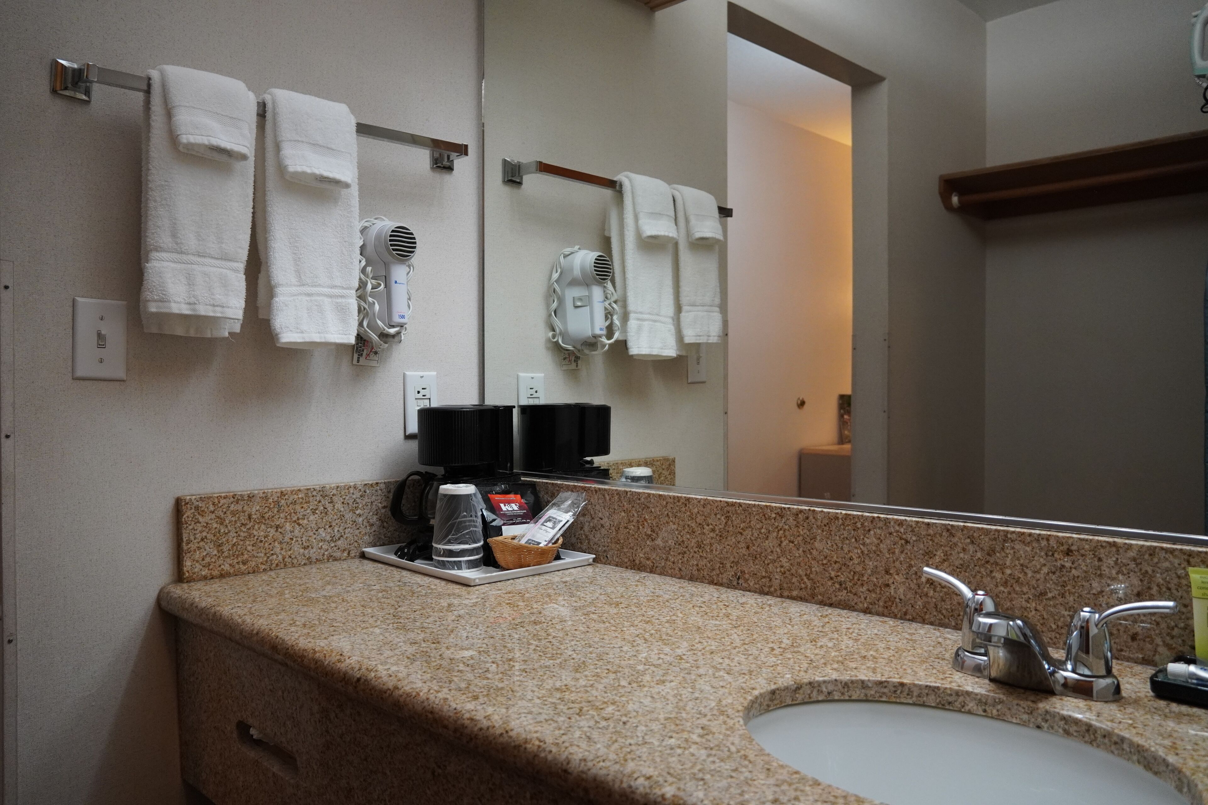 Un baño con encimera de granito, un lavabo, un espejo y toallas colgadas en un perchero.