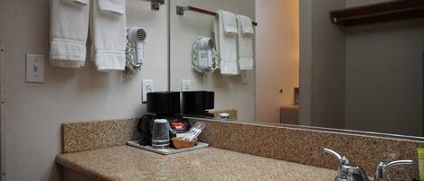 Un baño con encimera de granito, un lavabo, un espejo y toallas colgadas en un perchero.