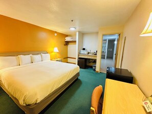 A hotel room with a large bed, a desk, a chair, a lamp, a microwave, and a trash bin. - Timberland Inn & Suites (Castle Rock)