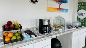 A kitchen counter with a coffee maker, fruit, and a painting of a tree.