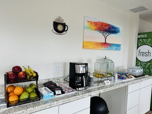 A kitchen counter with a coffee maker, fruit, and a painting of a tree. - Timberland Inn & Suites (Castle Rock)