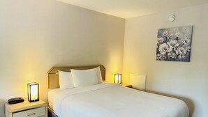 A neatly made bed with white linens, two bedside tables with lamps, a small drawer, and a wall-mounted painting of flowers. - Timberland Inn & Suites (Castle Rock)