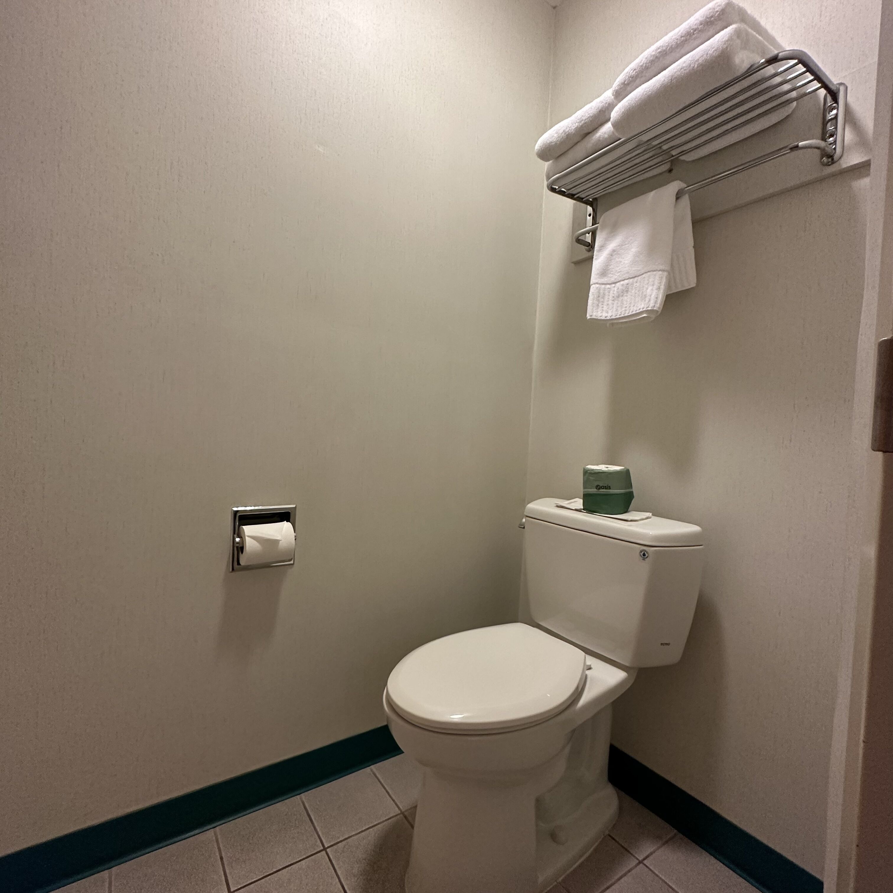 A bathroom with a toilet, a towel rack with towels, and a toilet paper holder.