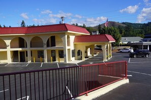 A building with a red roof and multiple arches, a parking lot, and a mountain in the background. - Timberland Inn & Suites (Castle Rock)
