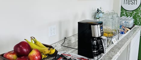 A kitchen counter with a coffee maker, a fruit basket, and a painting on the wall.