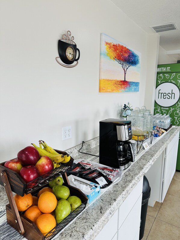 A kitchen counter with a coffee maker, a fruit basket, and a painting on the wall.