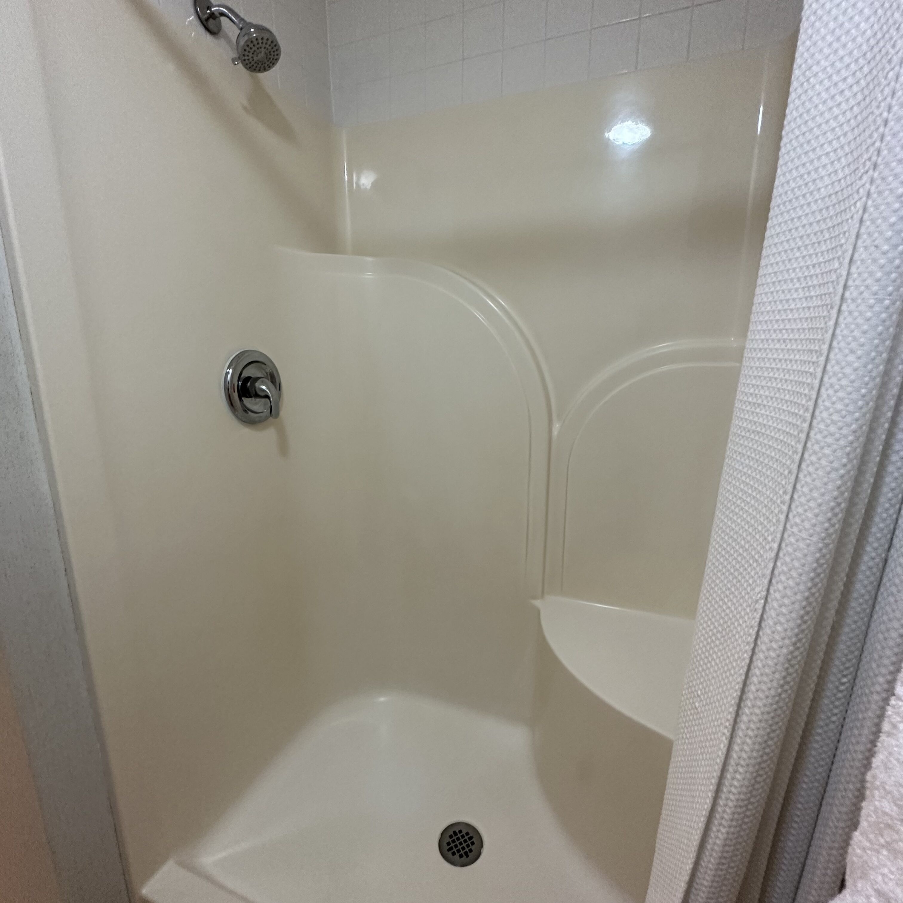 Eine Dusche mit Duschbrause, Ablaufrinne und Ablagefläche in der Ecke.