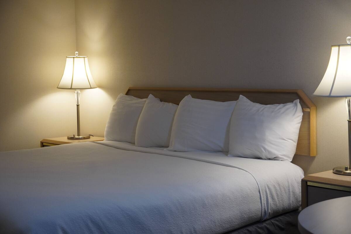 A neatly made bed with white linens, two bedside tables with lamps, and a wooden headboard.