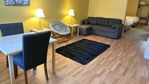 A modern living room with a dining area, a gray sofa, two lamps, and a painting on the wall. - Timberland Inn & Suites (Castle Rock)