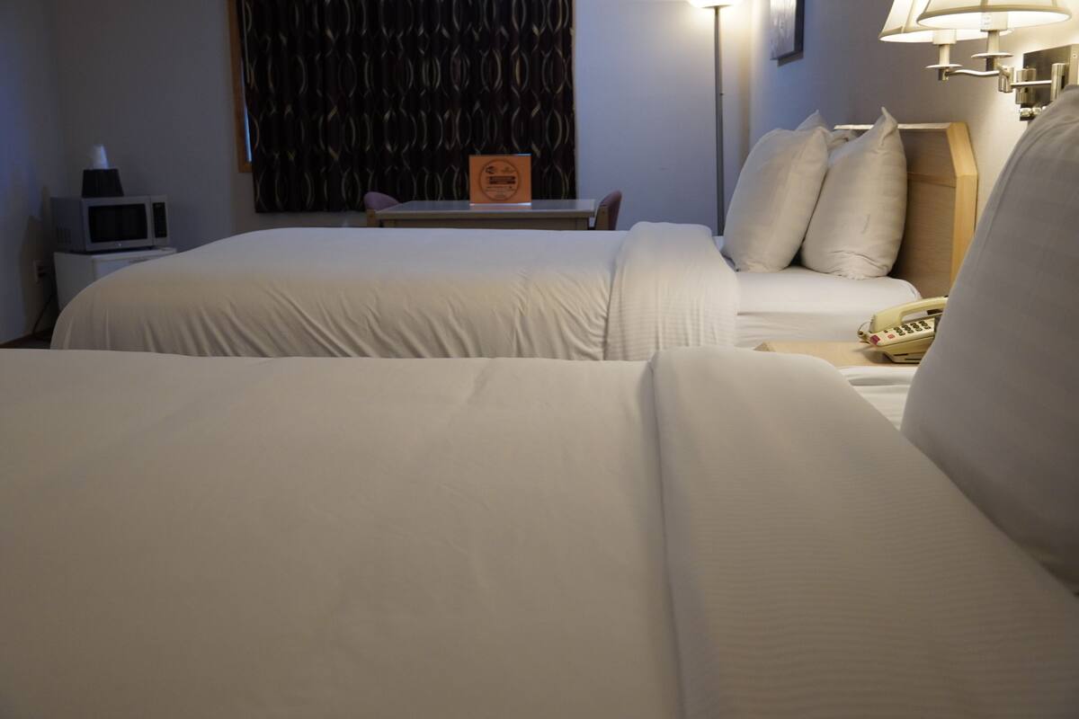 A hotel room with two beds, a desk with a lamp, a telephone, and a microwave.