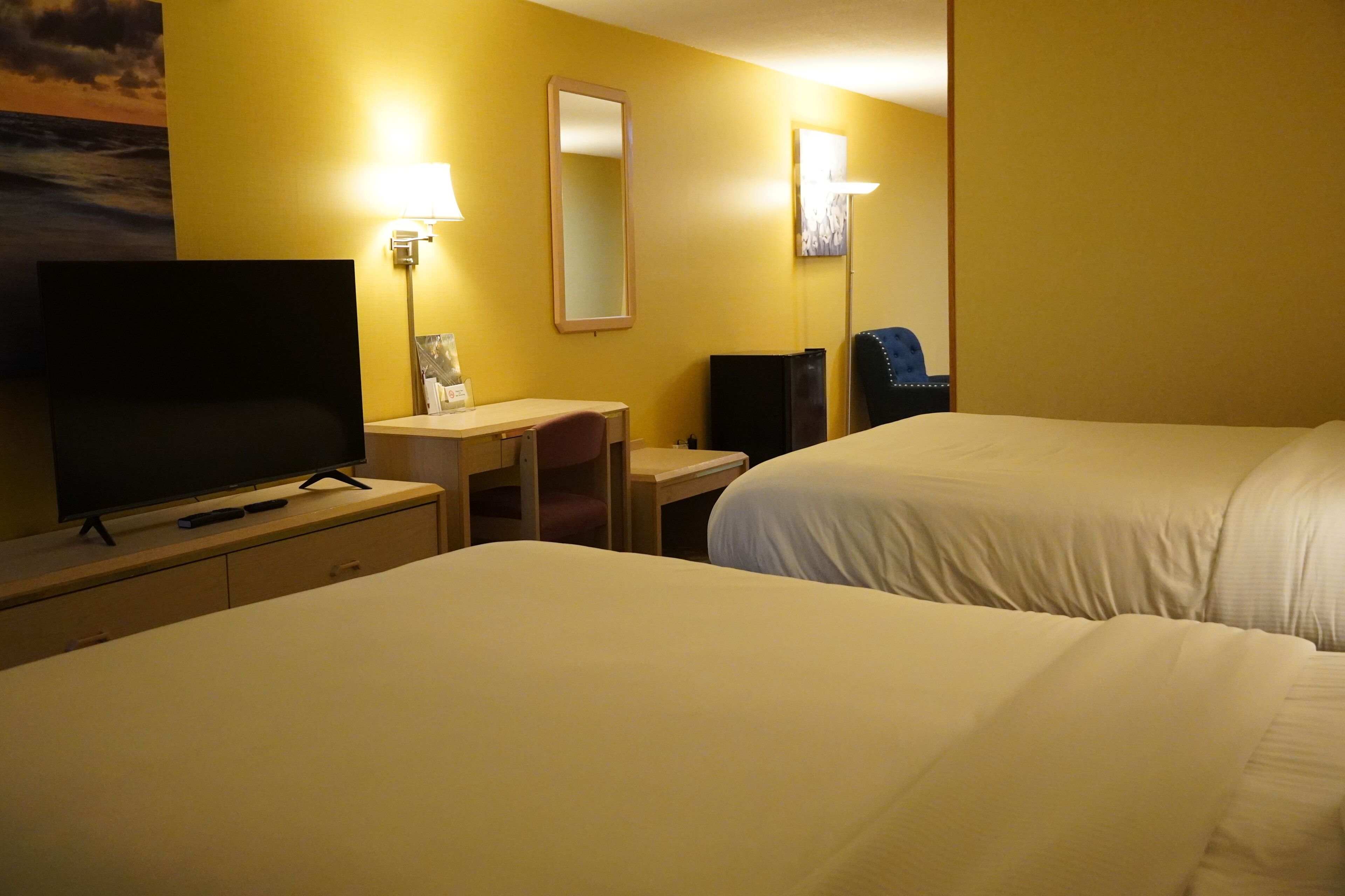 A hotel room with two beds, a desk, a chair, a television, and a mirror.