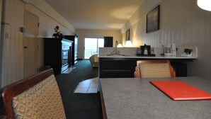 A hotel room with a dining area, kitchenette, and a view through the door. - Hillside Inn (Madison)