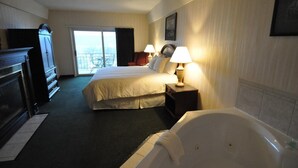 A hotel room with a large bed, a separate bed, a sitting area with a chair, a desk, a fireplace, and a view of the outdoors. - Hillside Inn (Madison)