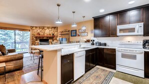 A modern kitchen with dark wood cabinets, a white microwave, and a built-in oven. - Atrium Condominiums (Breckenridge)