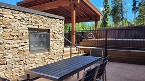 An outdoor patio with a stone wall, a wooden pergola, a grill, and a table with chairs. - Atrium Condominiums (Breckenridge)