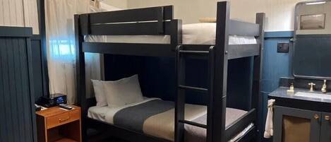 A bunk bed room with a small wooden nightstand, a mirror cabinet, and a ceiling light fixture.