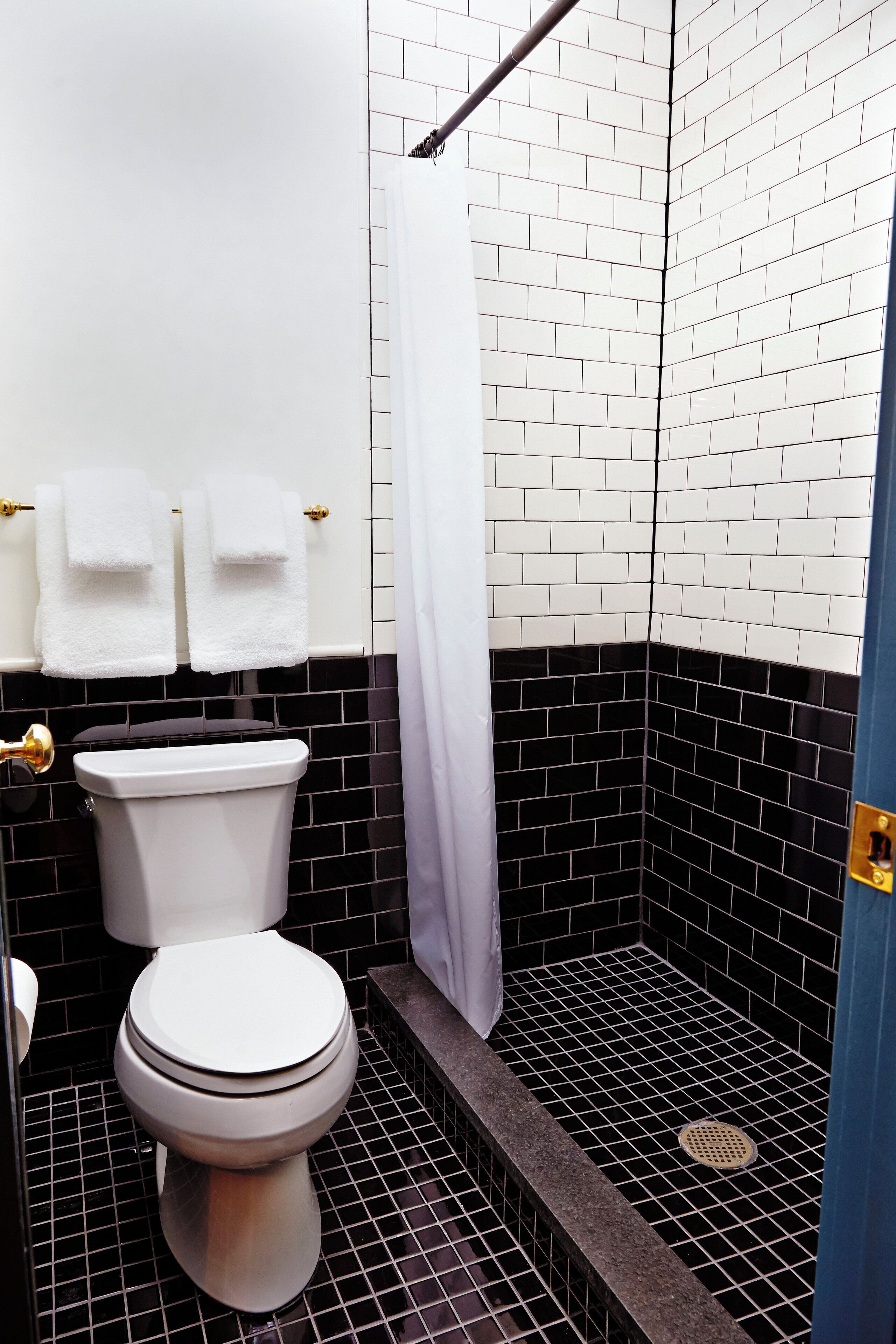A bathroom with a white toilet, black and white tiled walls, and a shower area.