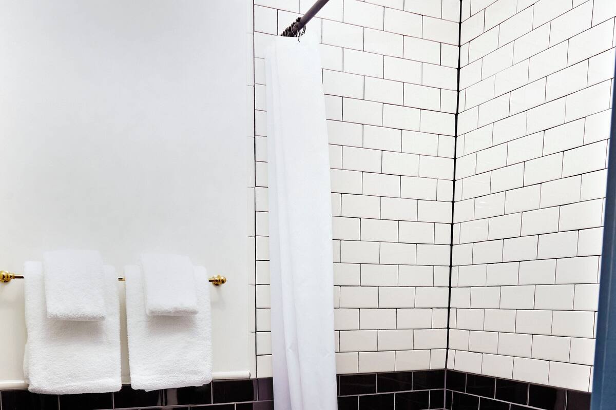 Une salle de bain avec des toilettes blanches, des murs carrelés en noir et blanc et un espace douche.