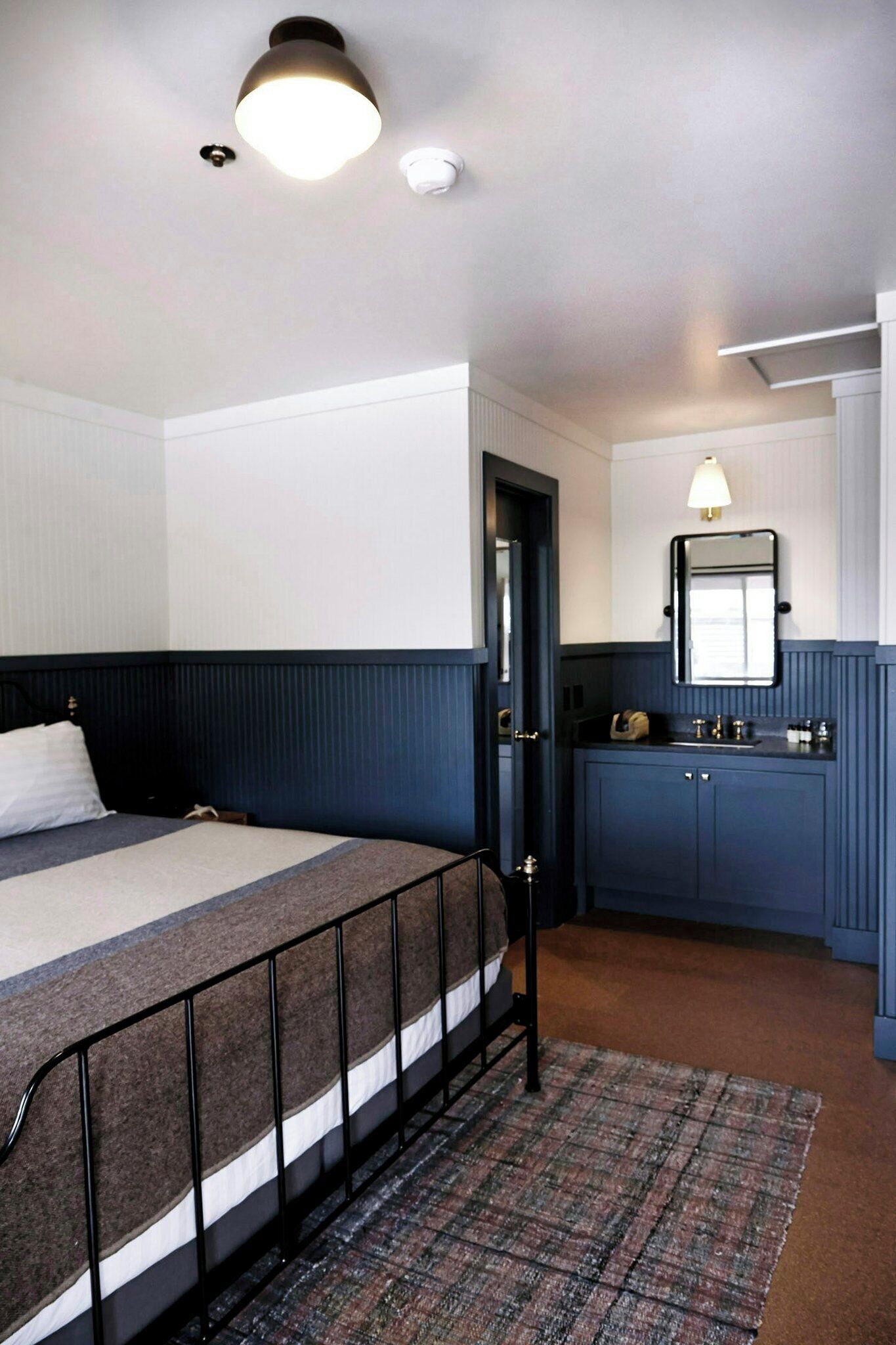 Une chambre à coucher comprenant un lit, une table de chevet, une commode, un miroir et une porte.