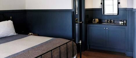A bedroom with a bed, a bedside table, a dresser, a mirror, and a door.