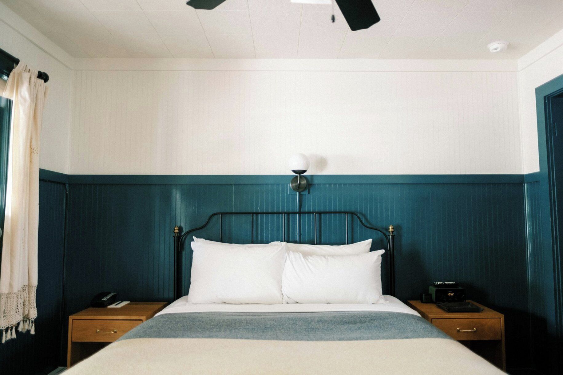 A bed with a white comforter and pillows, a bedside table with a lamp, and a nightstand with a phone.