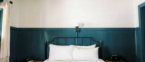 A bed with a white comforter and pillows, a bedside table with a lamp, and a nightstand with a phone.