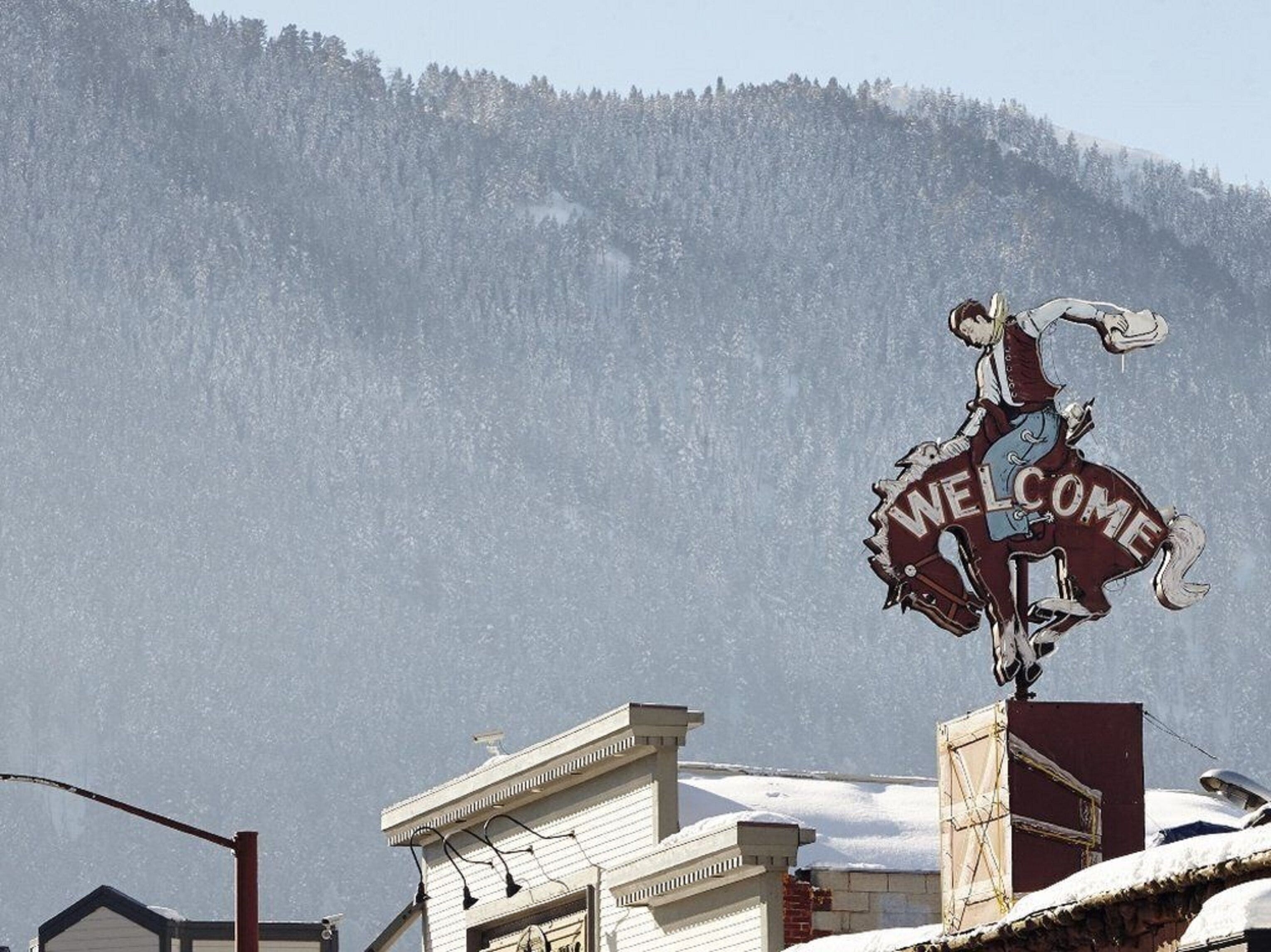 Une pancarte indiquant « BIENVENUE » est placée sur une statue de cheval dans une ville enneigée, avec une montagne en arrière-plan.