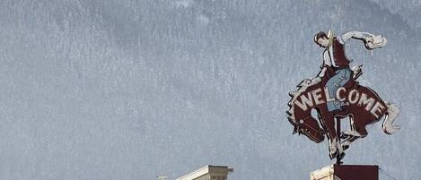 Une pancarte indiquant « BIENVENUE » est placée sur une statue de cheval dans une ville enneigée, avec une montagne en arrière-plan.
