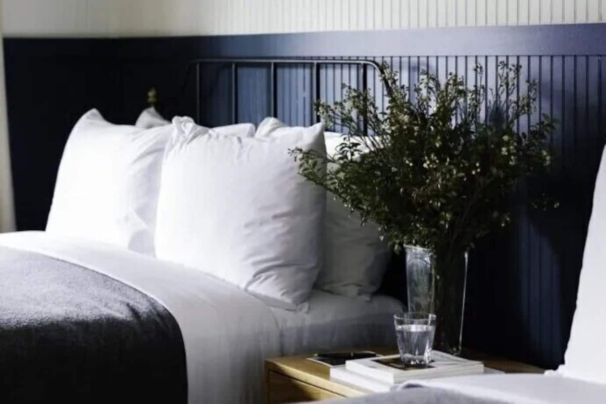 A neatly made bed with white linens, a vase with greenery, and a glass of water on a bedside table.