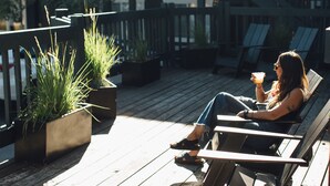 Una terraza de madera con asientos exteriores, plantas en macetas y barandilla.