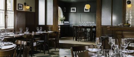 Un restaurante con mobiliario de madera, suelo de cuadros y una zona de bar con vasos y botellas.