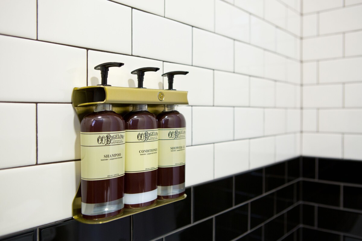 Tres botellas de champú y acondicionador sobre una repisa frente a una pared de azulejos.