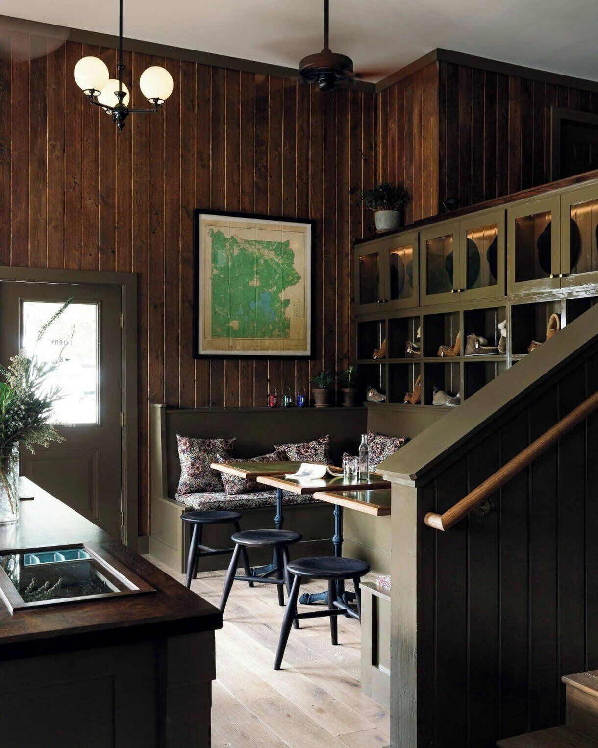 A wooden-paneled room with a dining area, a map on the wall, and a staircase with shoe storage.