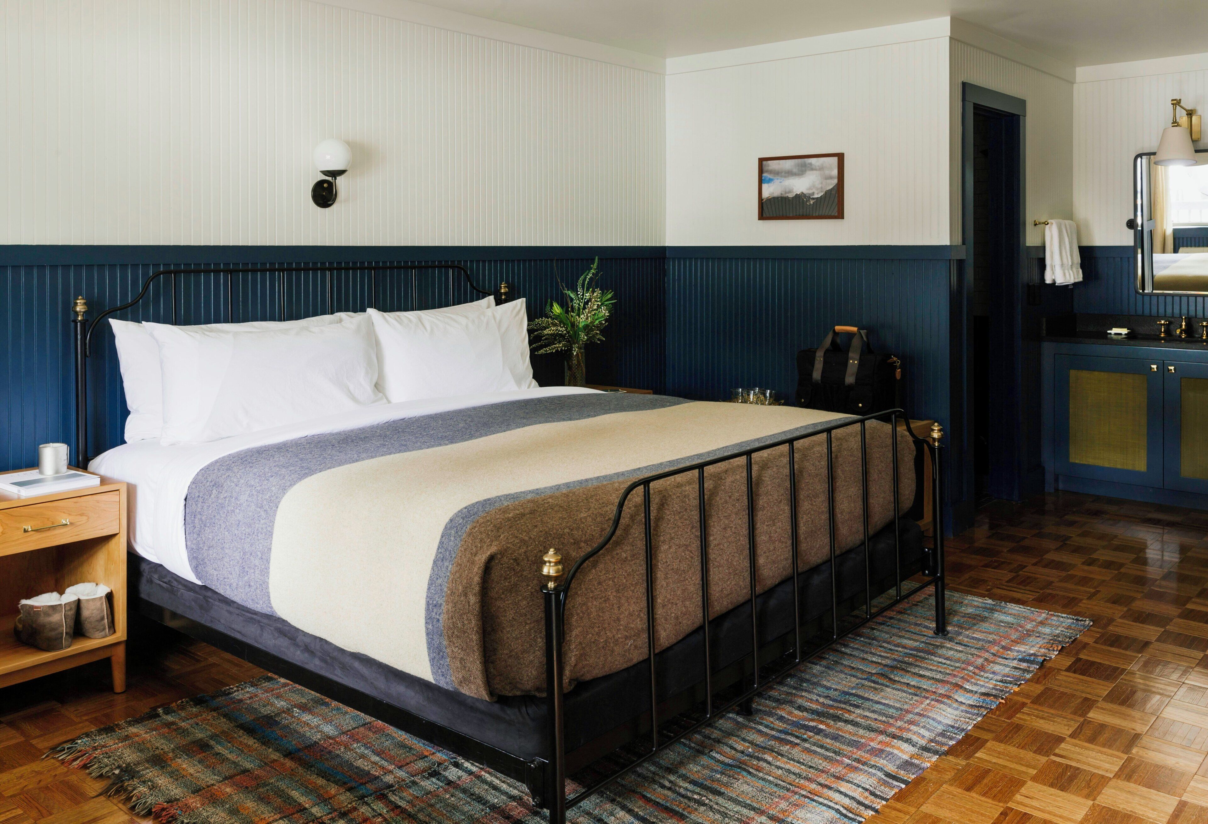 Een netjes opgemaakte slaapkamer met een bed, nachtkastje, lamp en uitzicht op de badkamer.
