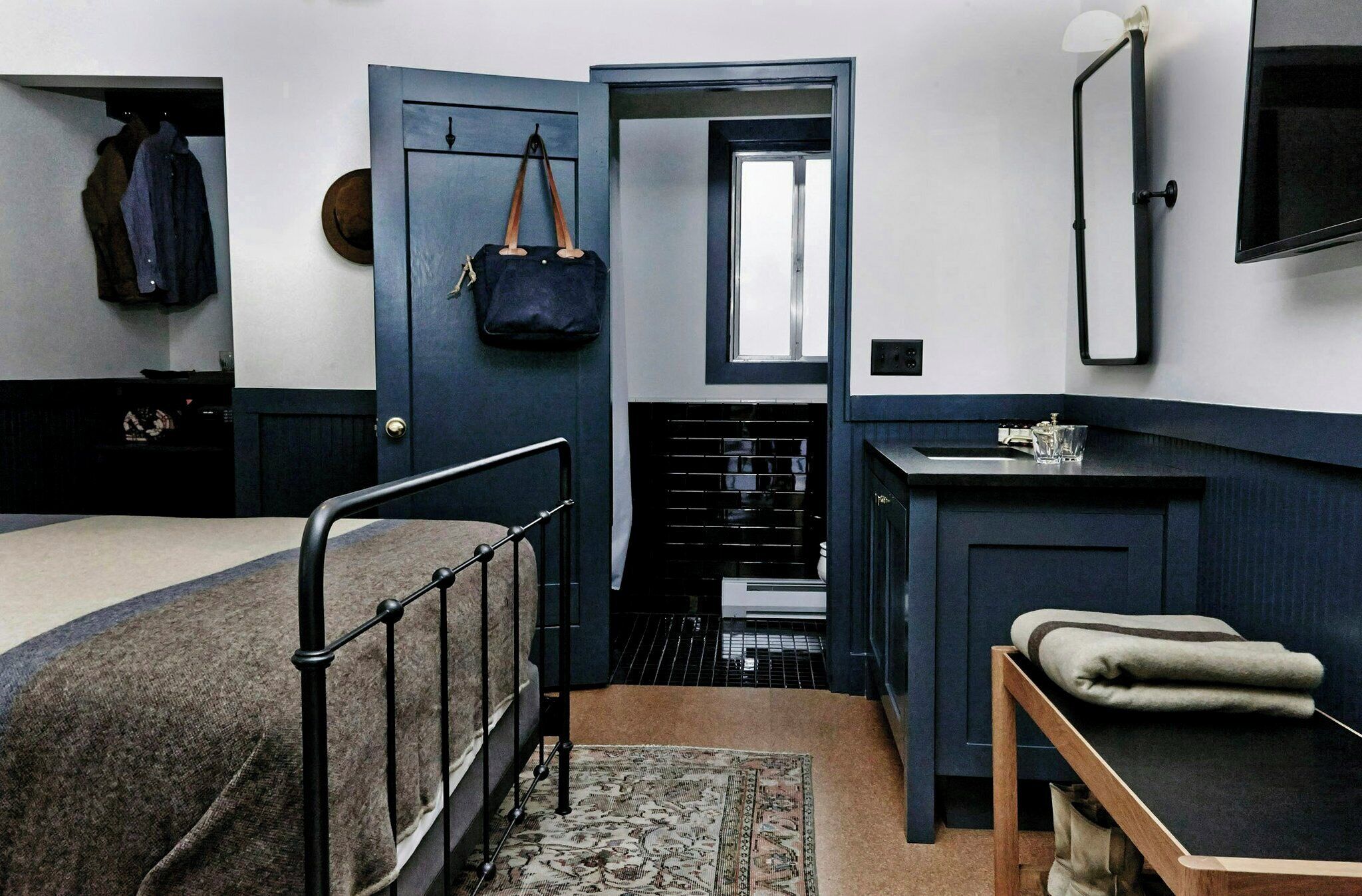 A bedroom with a bed, a bedside table, a mirror, a wardrobe, and a door leading to a bathroom.
