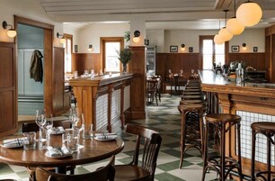 Restaurante com mobiliário de madeira, chão quadriculado e iluminação pendente.