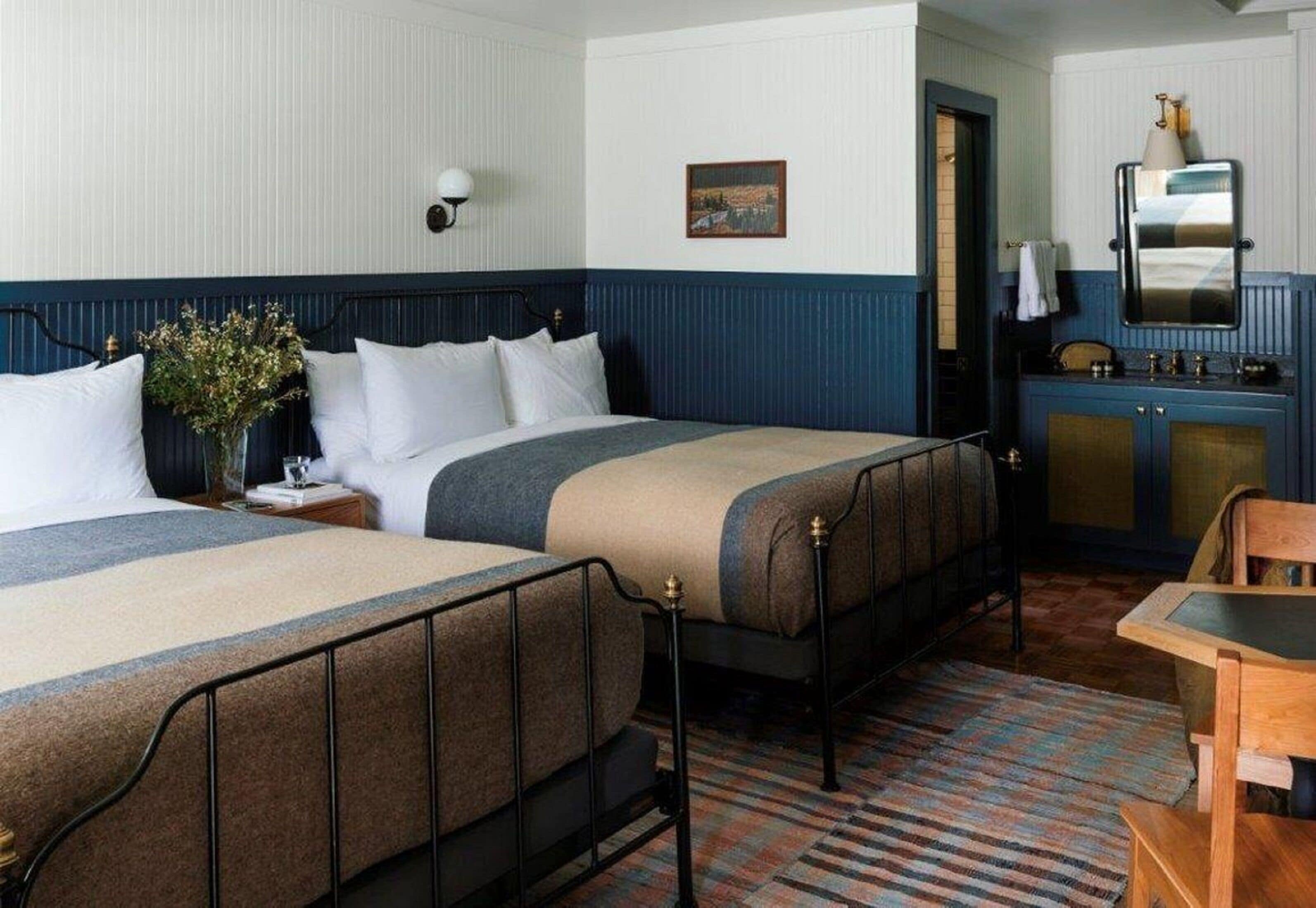A room with two beds, a small table, a mirror, and a cabinet.