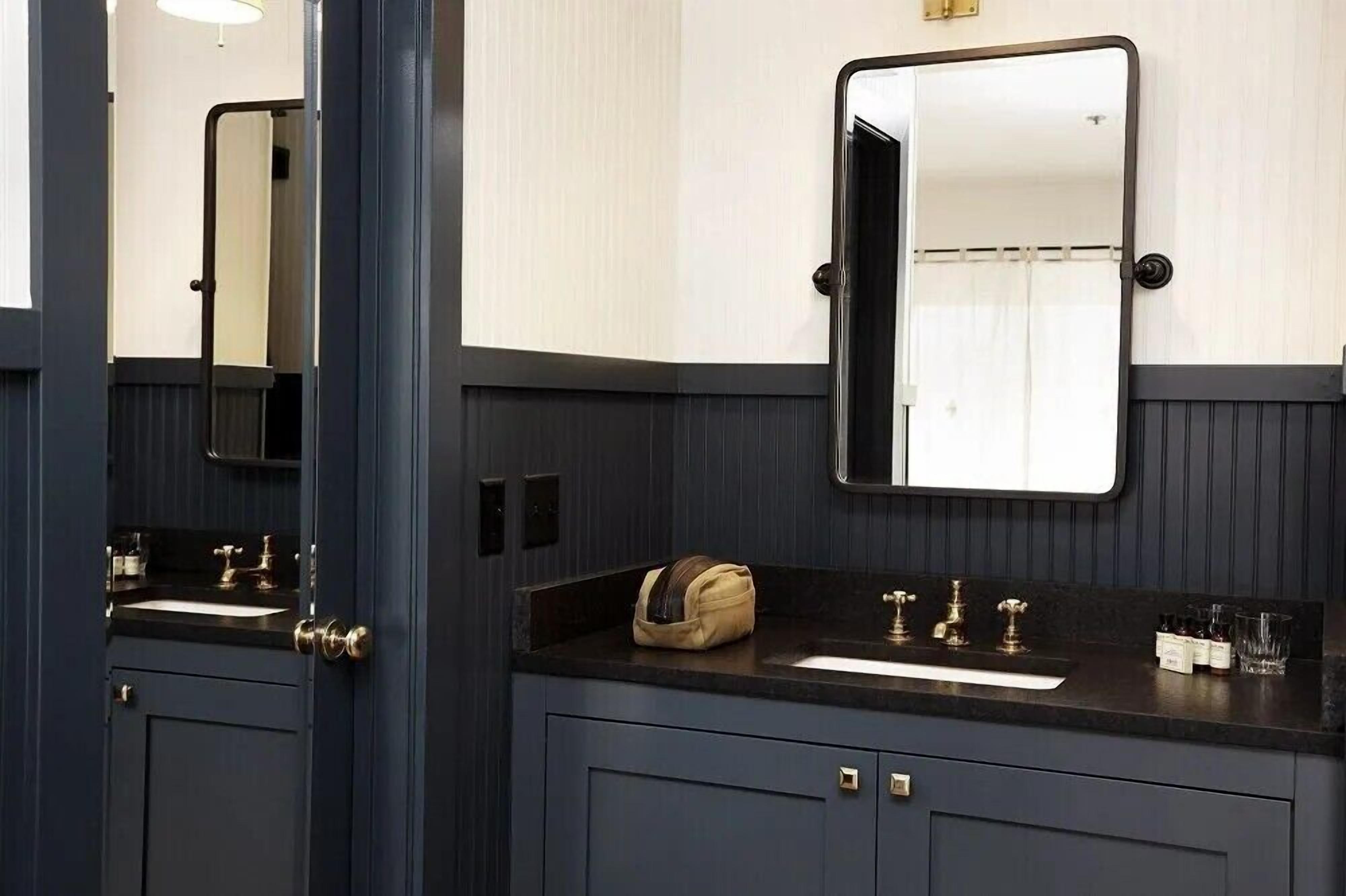 Un baño con tocador azul oscuro, un espejo, un lavabo y un perchero para toallas.