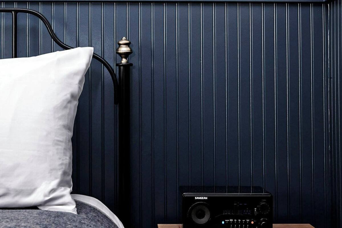 Une chambre à coucher avec un lit, une table de chevet dotée d’une radio et une commode en bois.