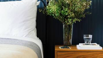 Una cama bien hecha con una almohada blanca, una mesita de noche con un florero de flores, un vaso de agua y un par de zapatos en el suelo.