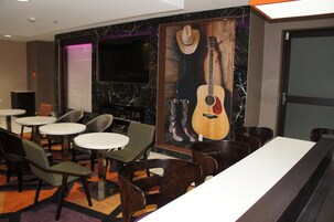 A restaurant with round tables and chairs, a large mural of a guitar and cowboy boots, and a dark-colored wall with a marble-like pattern.