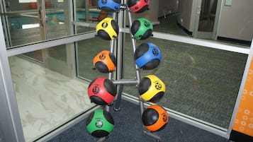 Una estructura con pelotas de ejercicio de diferentes pesos y colores, ubicada en una habitación con pared de vidrio y piso de baldosas.