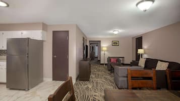 Una habitación de hotel moderna con kitchenette, zona de comedor y sala de estar con sofá y televisor.