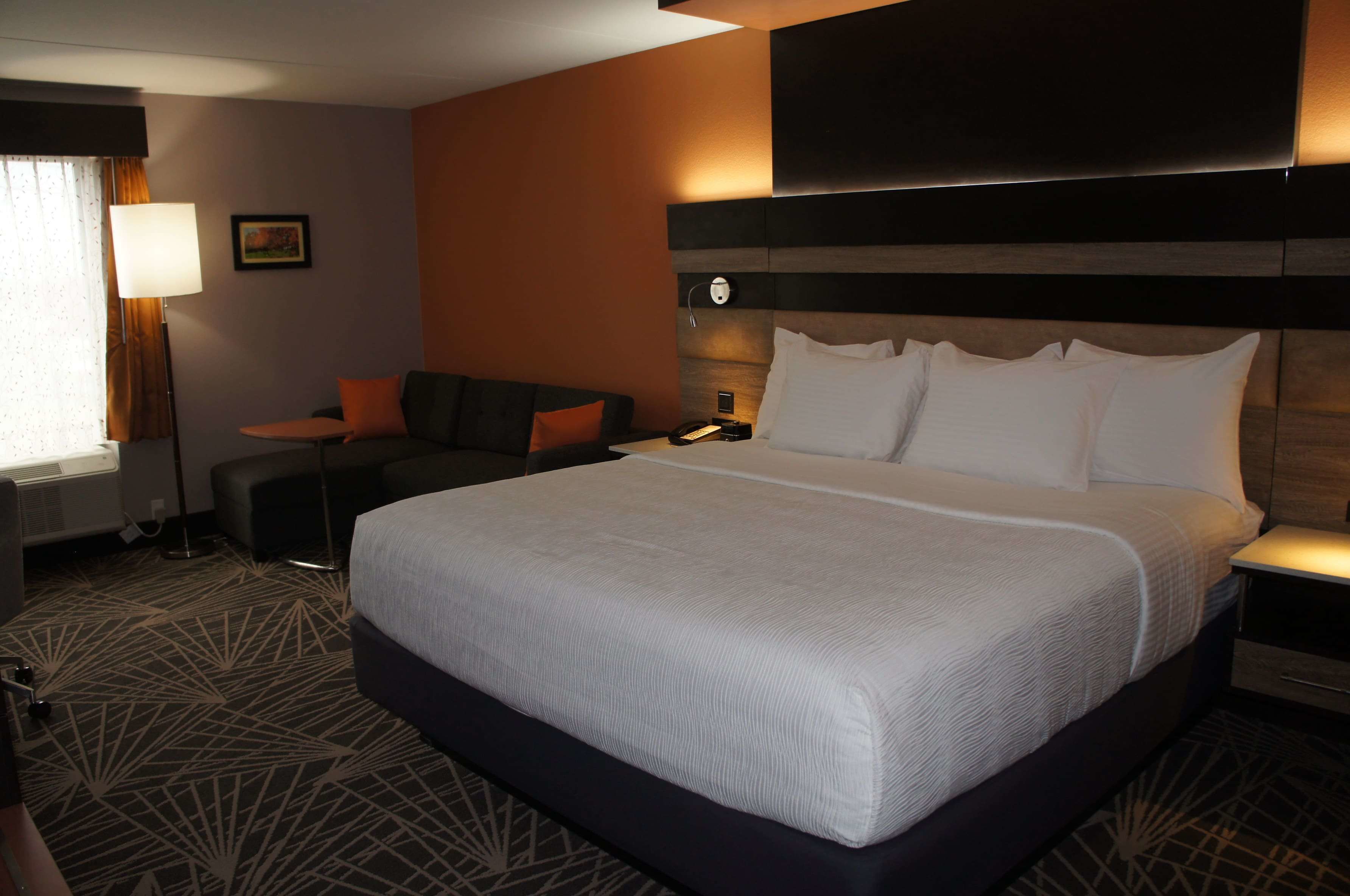 A hotel room with a large bed, a sofa, a desk, and a lamp.