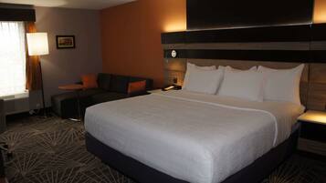 A hotel room with a large bed, a sofa, a desk, and a lamp.