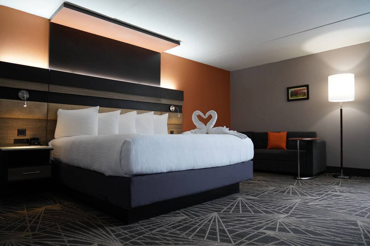 A hotel room with a large bed, a nightstand, a desk, a sofa, and a floor lamp.