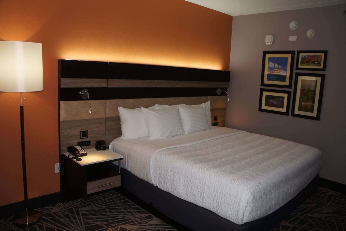 A hotel room with a large bed, a bedside table with a lamp, a phone, and a small drawer. There are framed pictures on the wall.