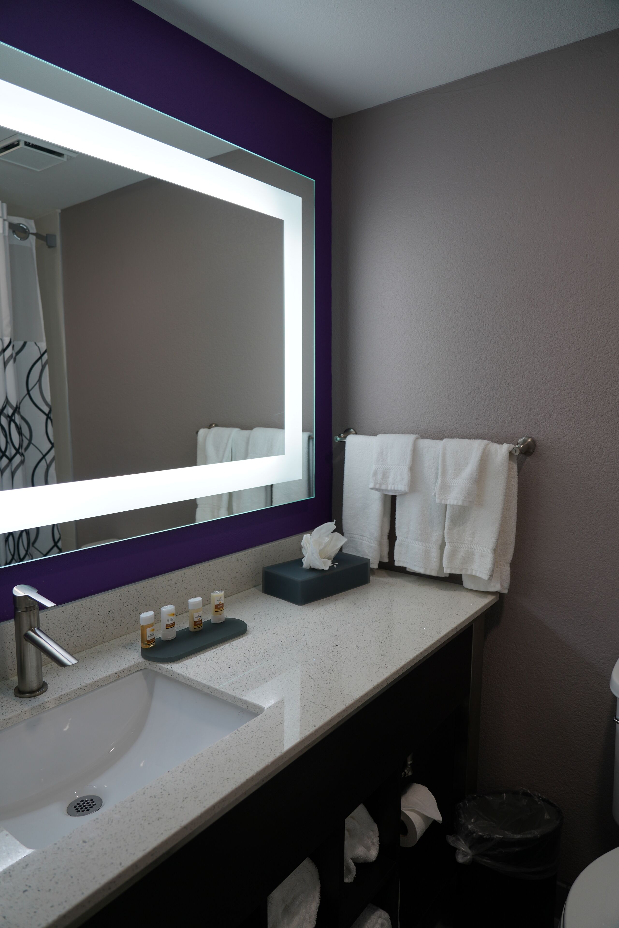A bathroom with a large mirror, a sink, and a towel rack.